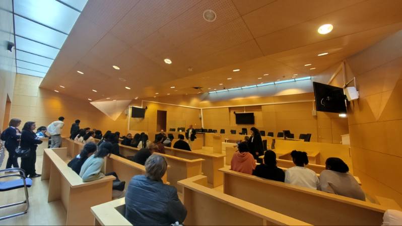Vue panoramique de la salle des Assises, avec les élèves répartis dans les bancs du public. L'aménagement montre une disposition avec une estrade pour les juges.