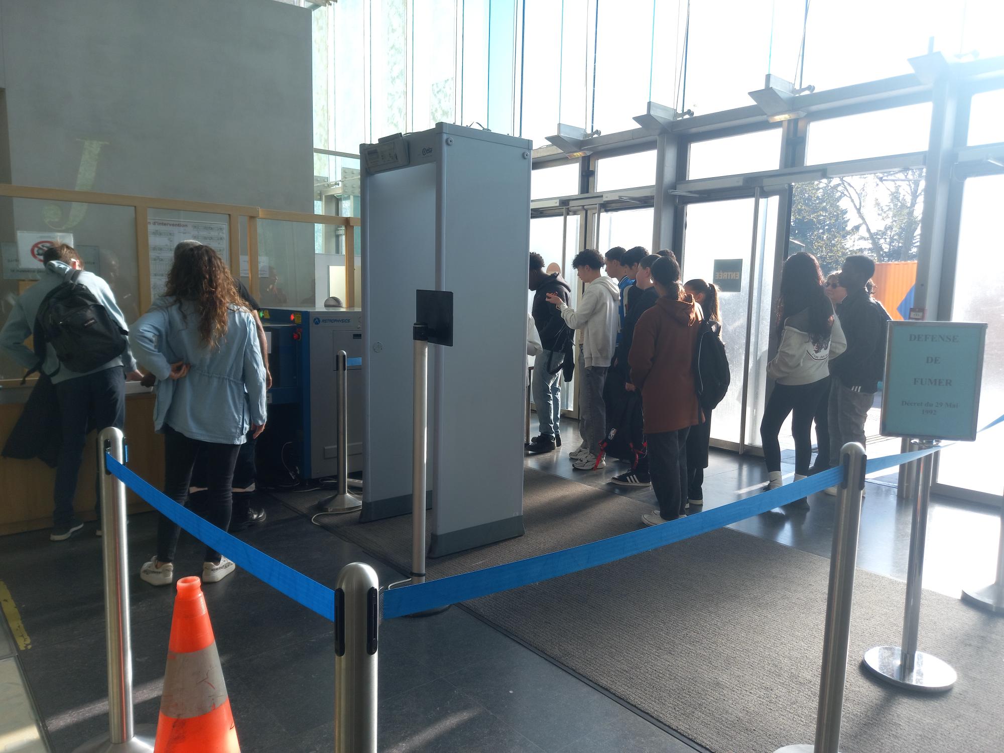 Les élèves passent le portique de sécurité dans le hall d'entrée du tribunal, encadrés par un personnel de sécurité.