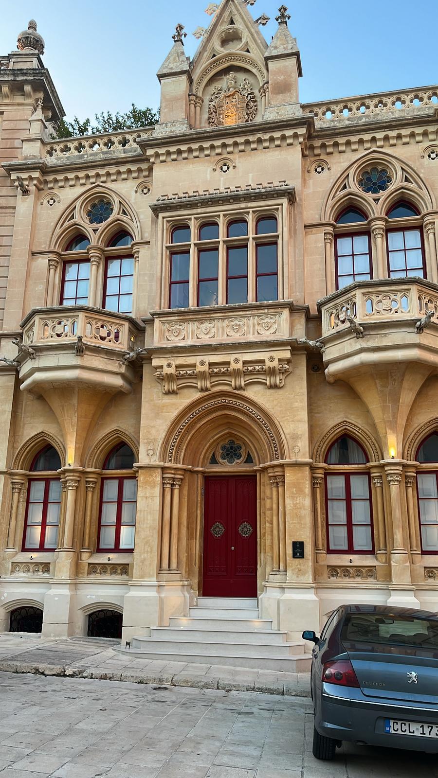 Maison noble de style néogothique, ornée d'arches et de balcons sculptés, aux fenêtres rouges caractéristiques.