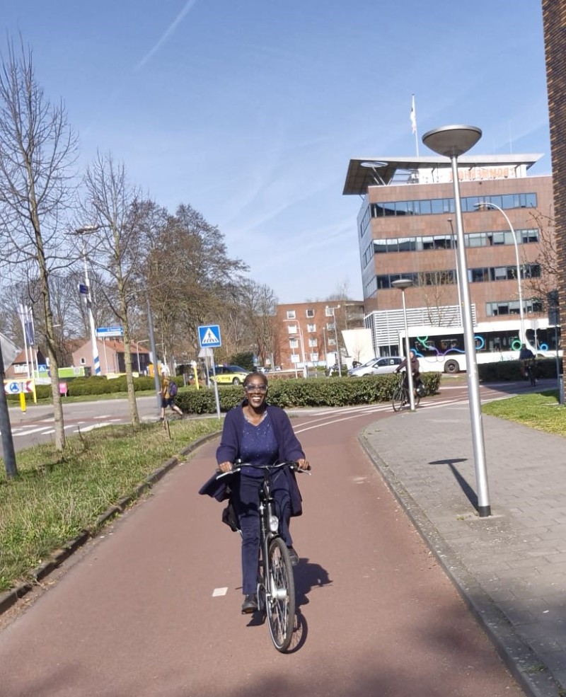L'image montre une des enseignantes de la délégation française, souriante et à vélo, qui circule sur une large piste cyclable à Zwolle.