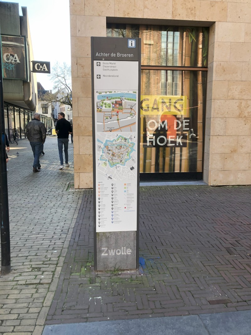 L'image montre la carte urbaine du quartier Broeren de Zwolle, un quartier animé avec des bâtiments modernes et historiques. Le paysage urbain comprend des rues pavées et des boutiques.