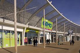 Vue extérieure du magasin Gémo à Lieusaint, avec une devanture lumineuse et moderne, où plusieurs clients entrent et sortent sous un toit en verre incurvé.